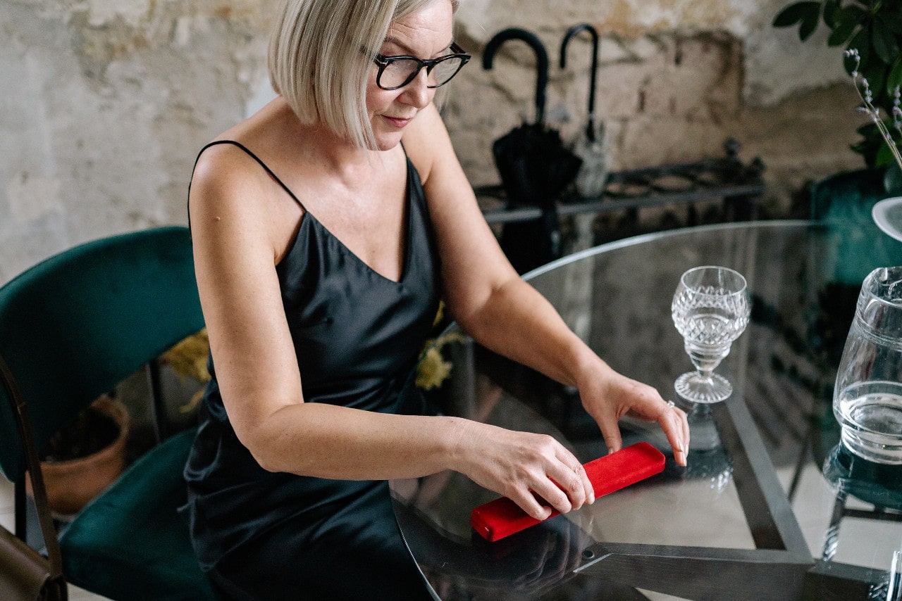 A woman holding a red necklace box at a glass dining table.