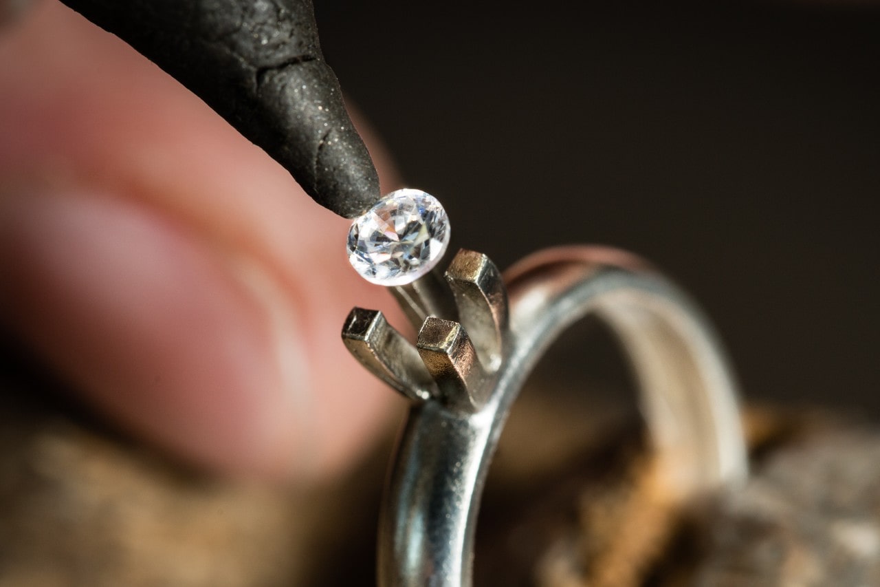 A close up of a jeweler inserting a diamond into the silver engagement ring setting