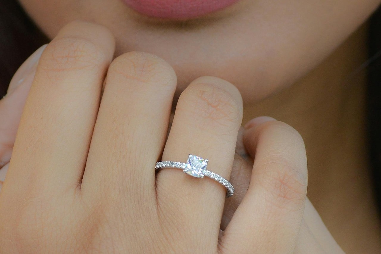 a woman’s hand raised to her face wearing a princess cut engagement ring