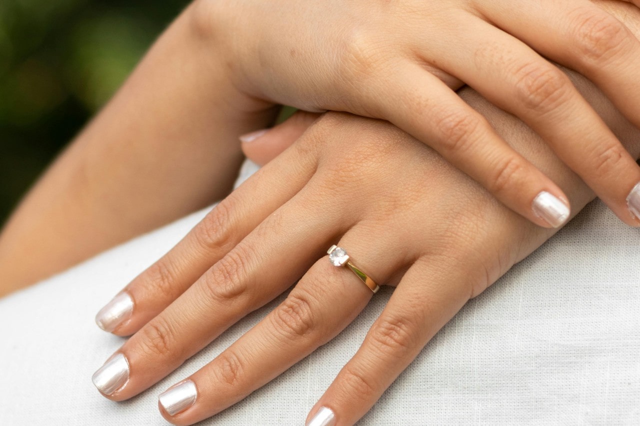 a woman’s hands crossed behind her partners shoulders, wearing a solitaire engagement ring