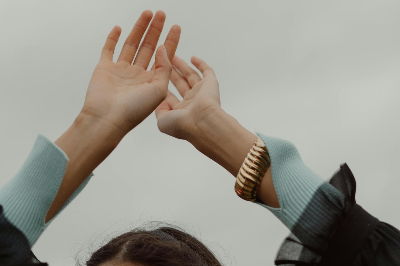 a woman’s hands raised in the air, wearing a chunky gold bangle