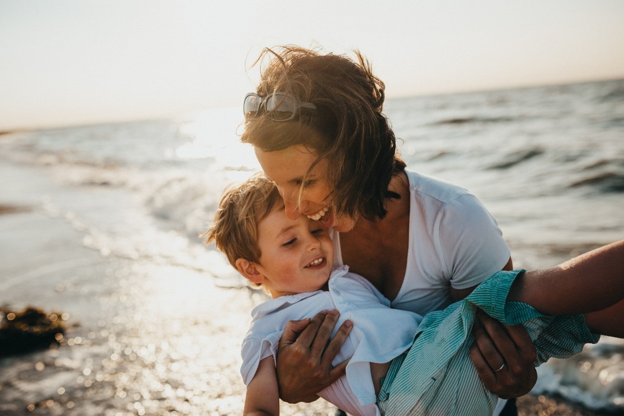 A joyful mother holding her son in her arms on the beach.