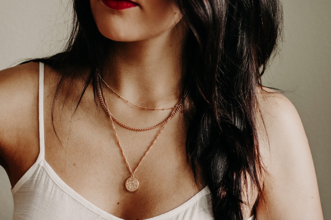 A close up of a women&rsquo;s necklace adorned with layered rose gold chain and pendant necklaces.