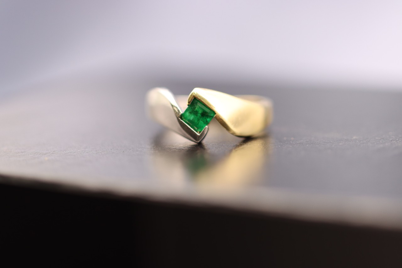 A yellow gold unconventional fashion ring with square emerald on a reflective surface