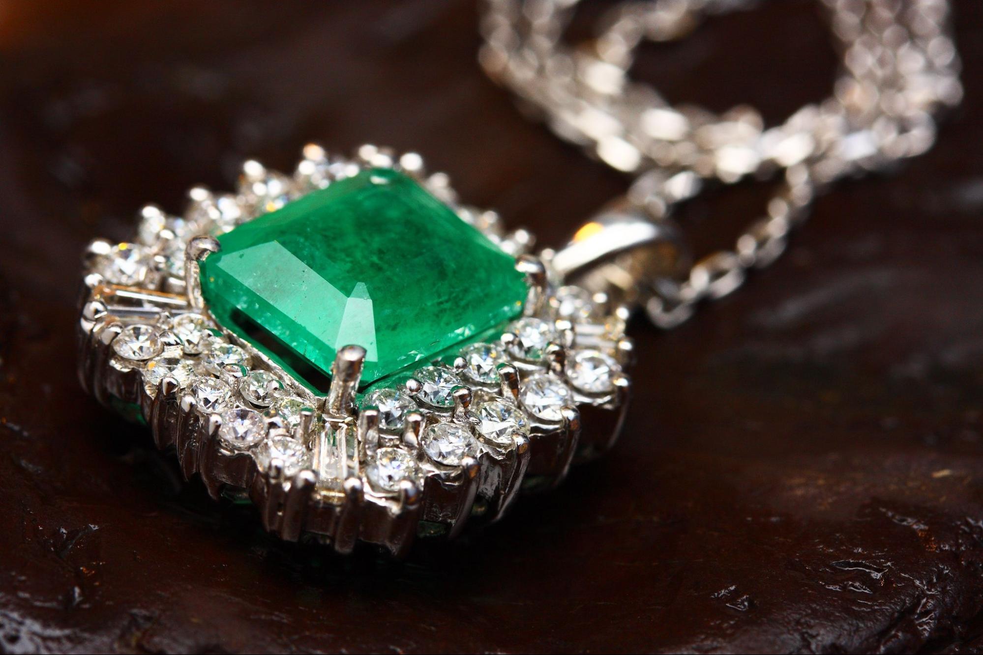 A white gold halo emerald pendant on a textured brown surface