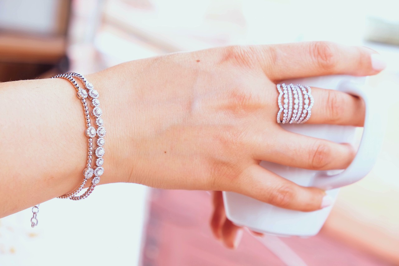 A close up of a woman's hand wearing white gold diamond bracelets and stackable diamond rings.