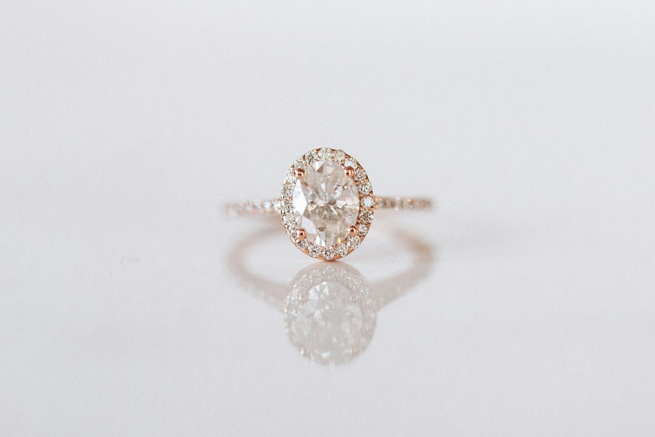 A rose gold oval halo engagement ring against a white background A rose gold oval halo engagement ring against a white background