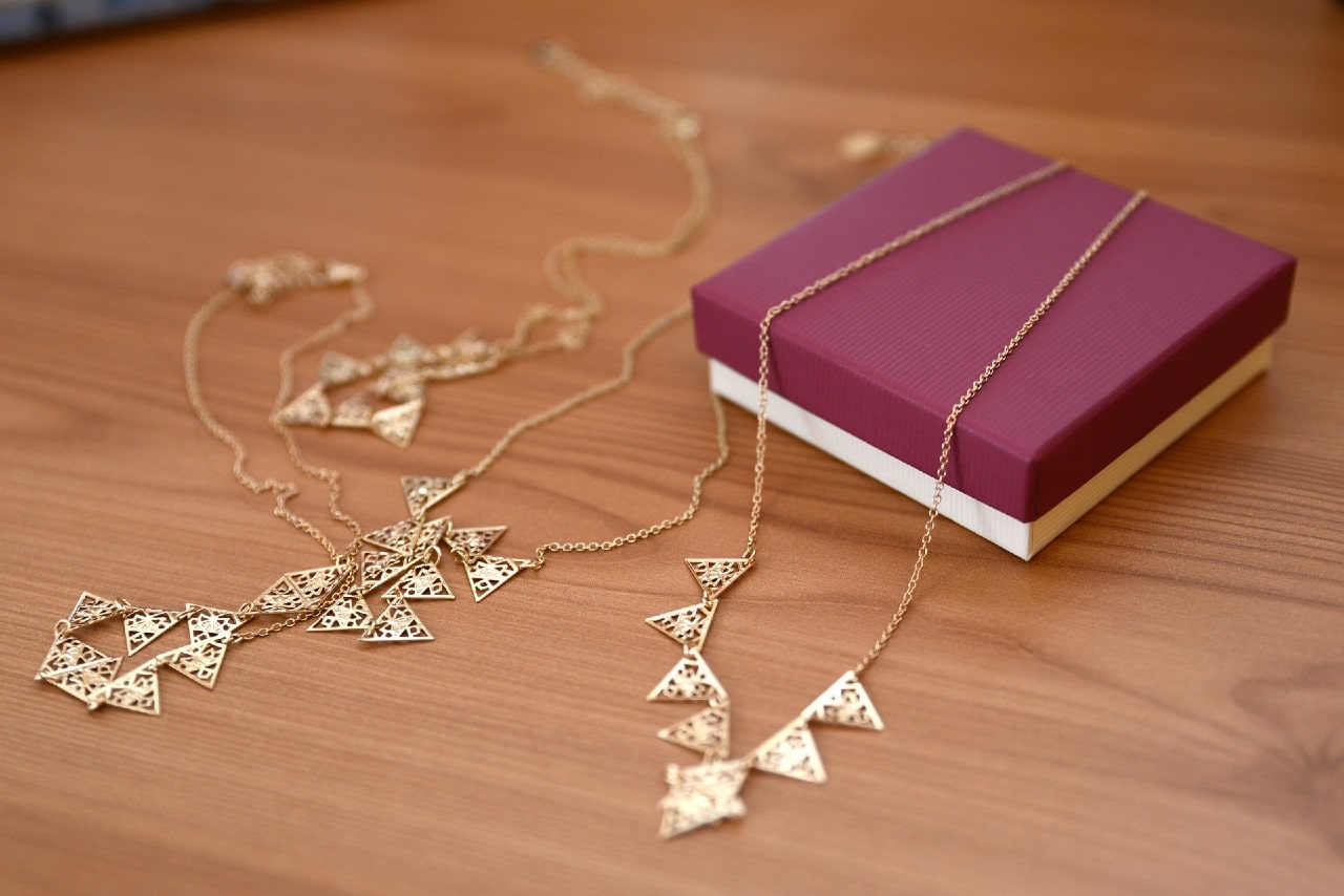 Gold necklaces lay scattered on a wooden surface beside a red small jewelry box. Gold necklaces lay scattered on a wooden surface beside a red small jewelry box.