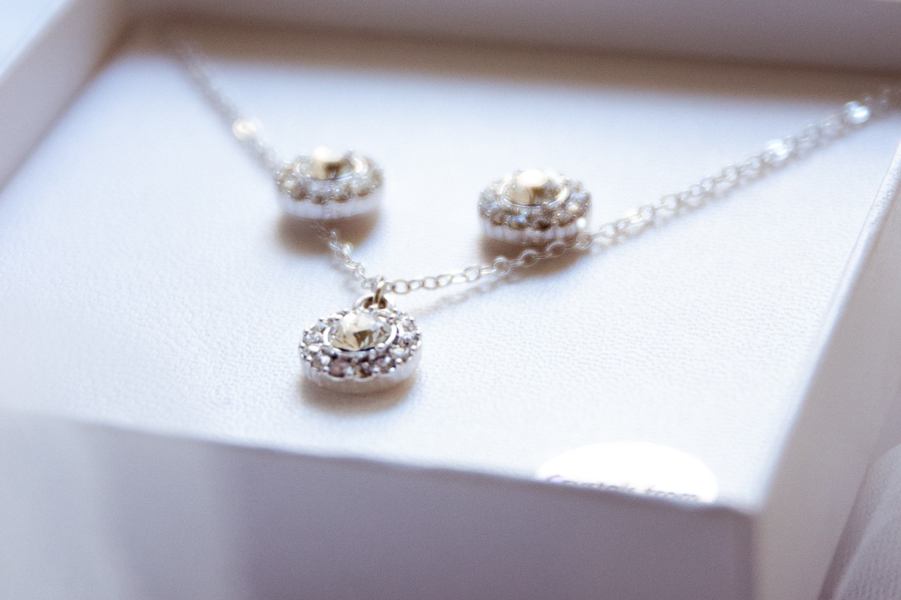 A diamond halo pendant with matching halo stud diamond earrings in a white box. A diamond halo pendant with matching halo stud diamond earrings in a white box.