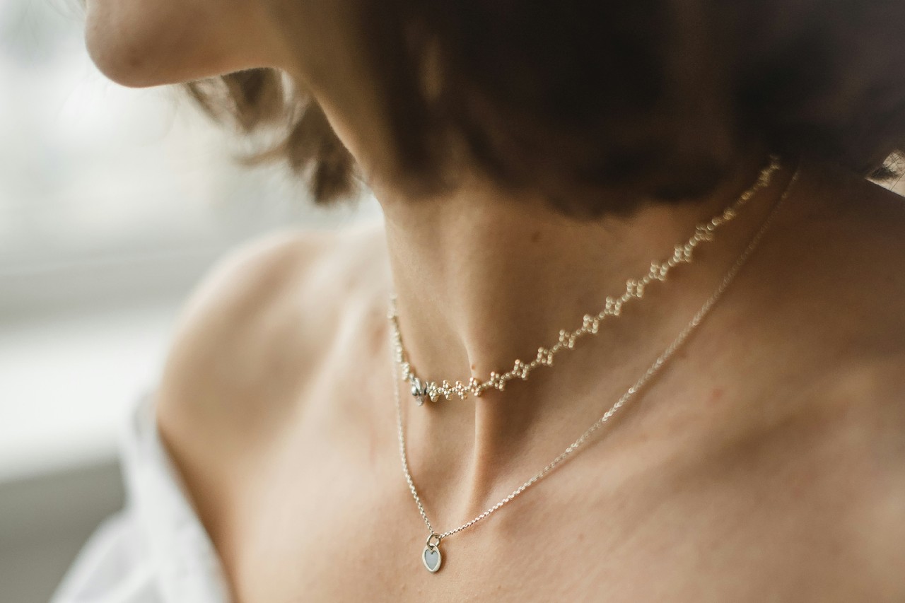 A close up of a woman with short hair, wearing a white strapless dress, adorned with two yellow gold necklaces: a simple chain and a heart-shaped pendant. A close up of a woman with short hair, wearing a white strapless dress, adorned with two yellow gold necklaces: a simple chain and a heart-shaped pendant.