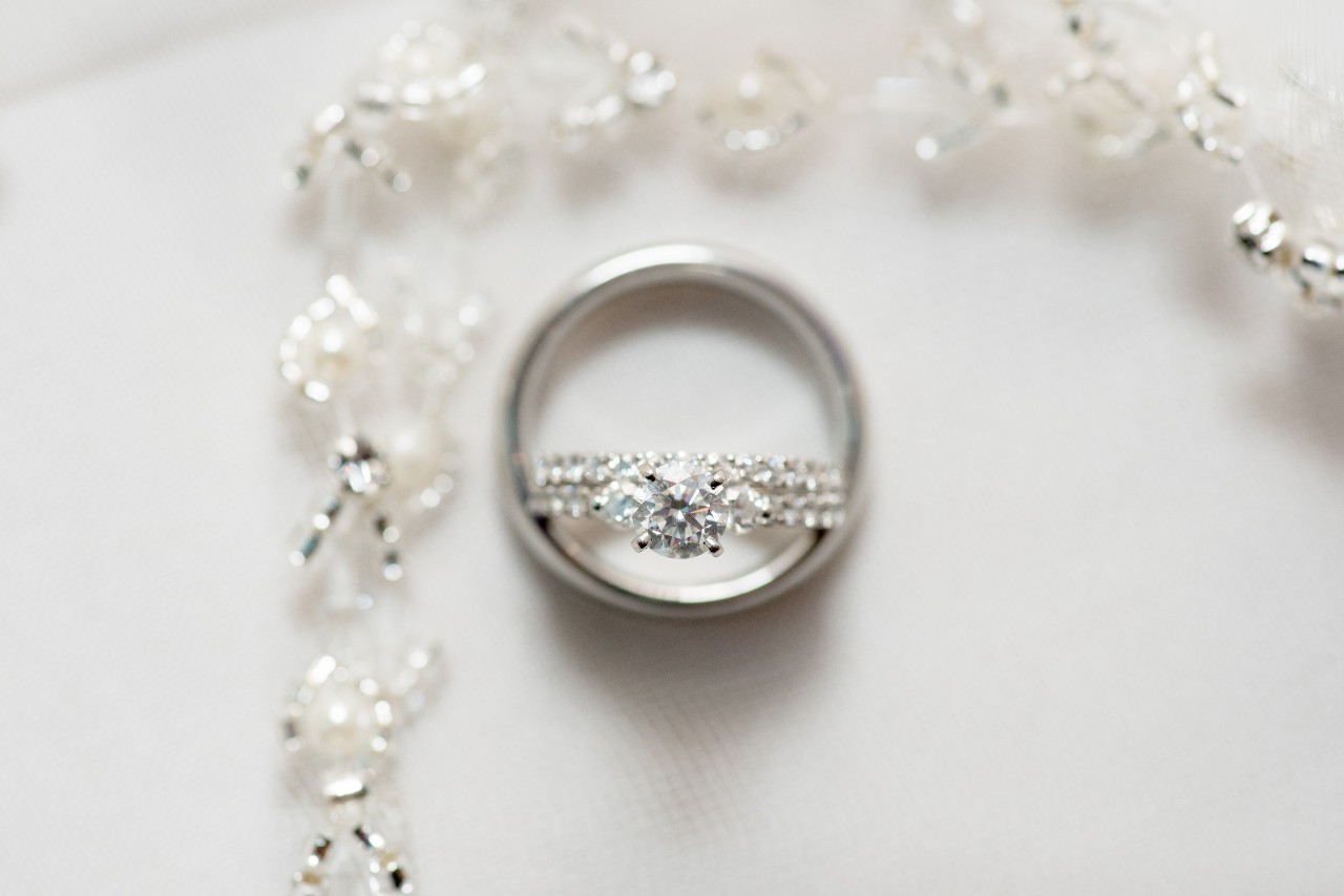 A close-up of a white gold triple row diamond engagement ring and polished wedding bands on a white surface.