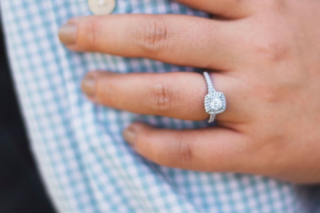 A close-up of a white gold diamond double halo side stone engagement ring on a checkered shirt.