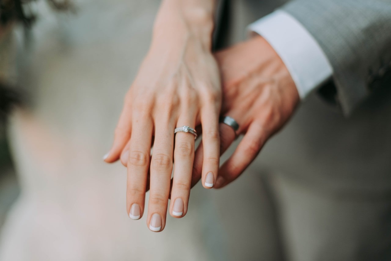 A bride and groom cross hands, showing off their wedding bands.