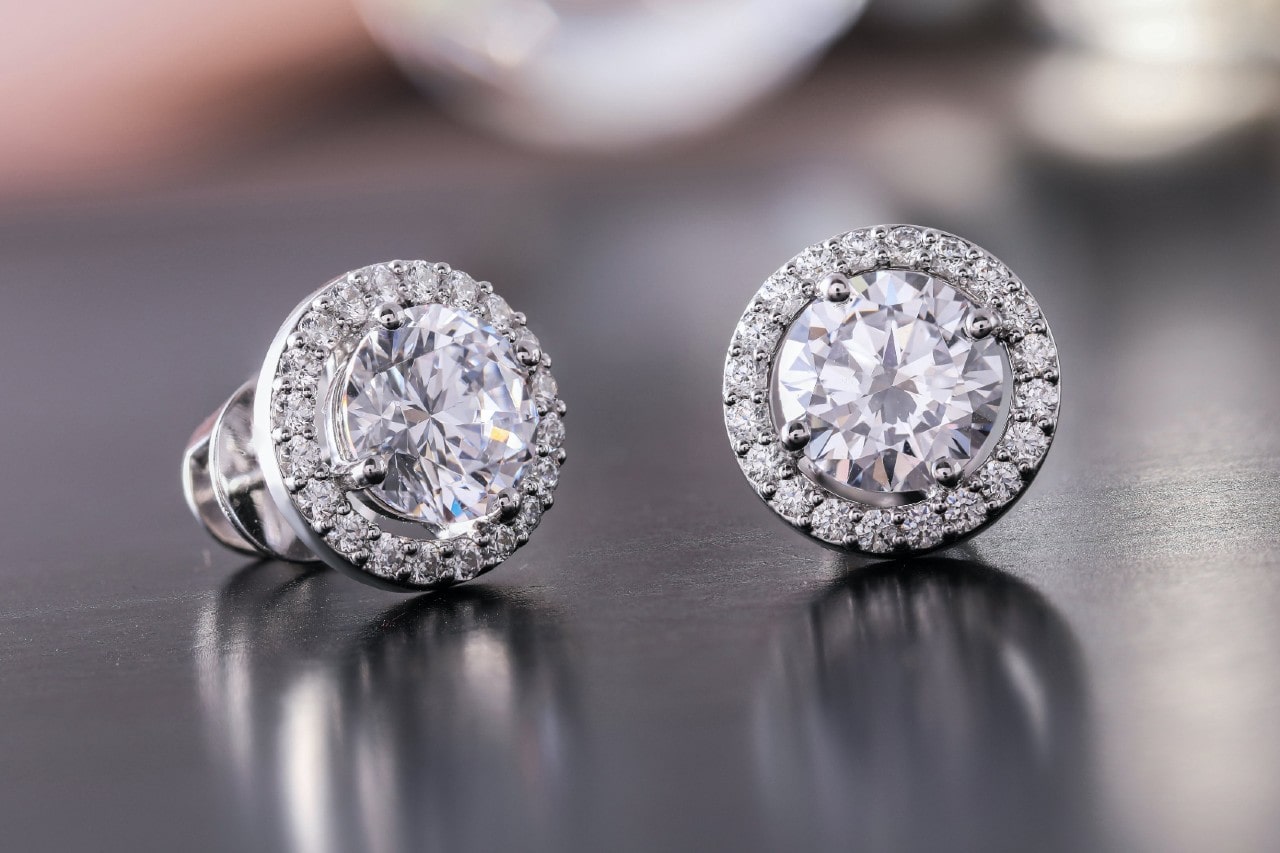 a pair of diamond halo stud earrings on a reflective metal surface a pair of diamond halo stud earrings on a reflective metal surface