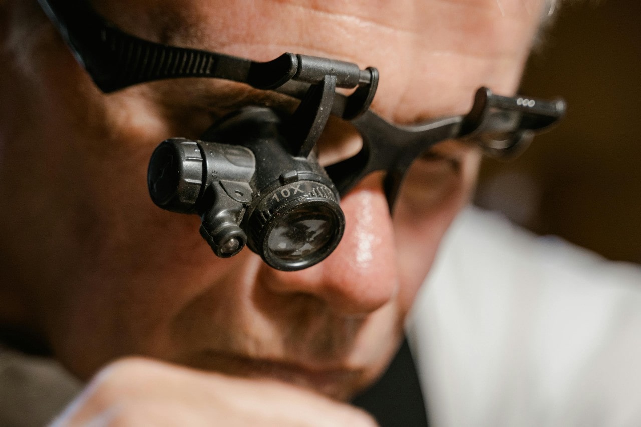 a jeweler looking through a magnifying glass, working on a project a jeweler looking through a magnifying glass, working on a project