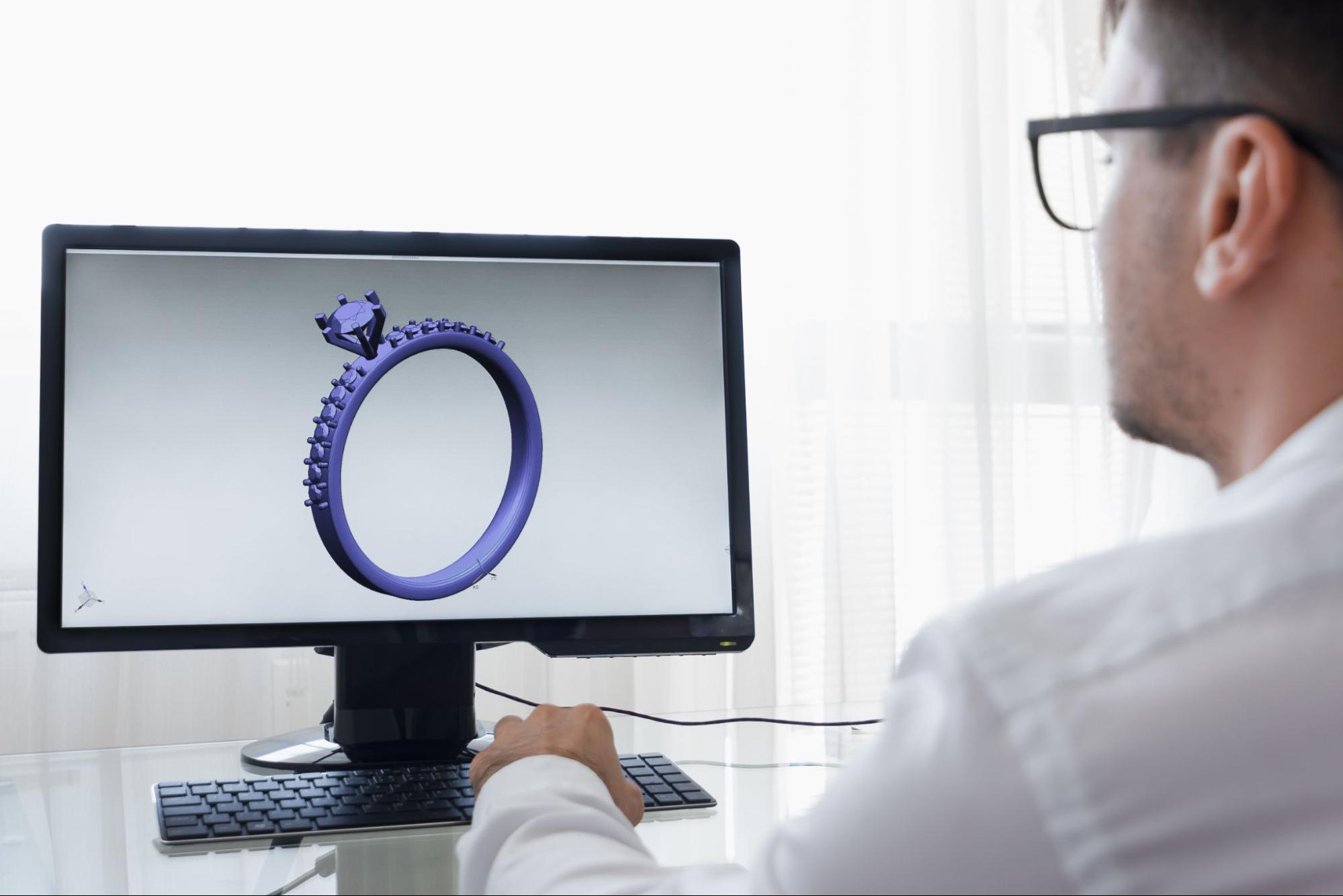 A jewelry expert creating a 3D design of an engagement ring on a computer, sitting in a bright room.