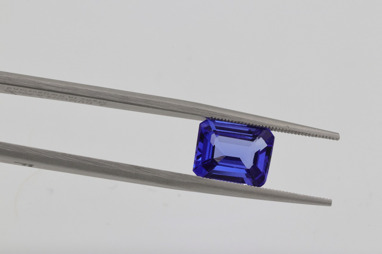 A close-up of a stunning sapphire held between the prongs of jeweler’s tweezers. A close-up of a stunning sapphire held between the prongs of jeweler’s tweezers.