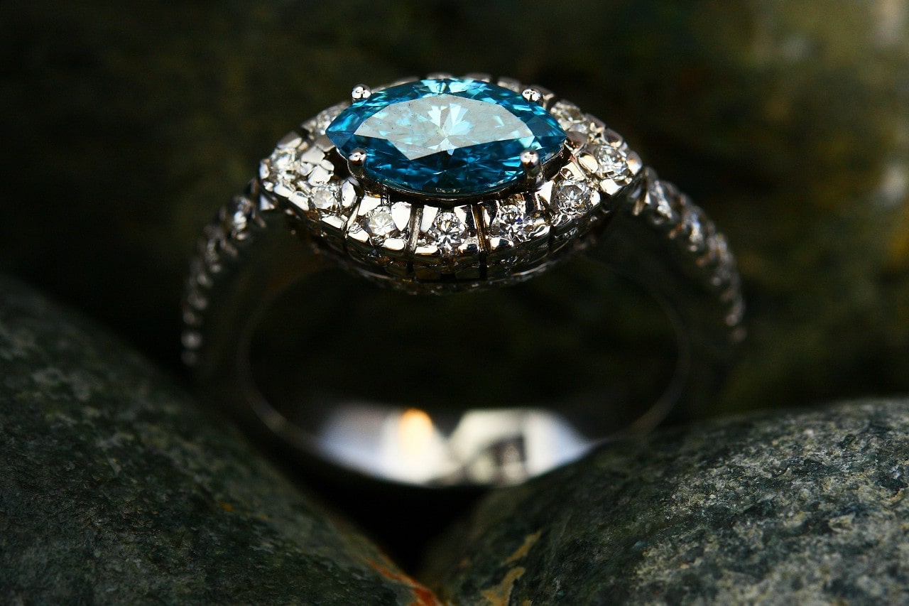 An elegant east-west engagement ring with a blue center stone and ornate diamond band. An elegant east-west engagement ring with a blue center stone and ornate diamond band.