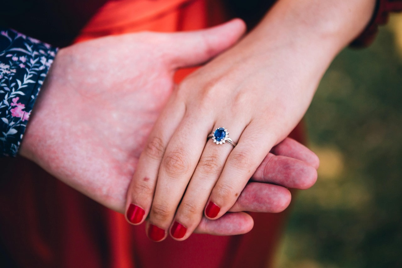 A couple holding hands, with emphasis on a white gold engagement ring with a sapphire center stone.