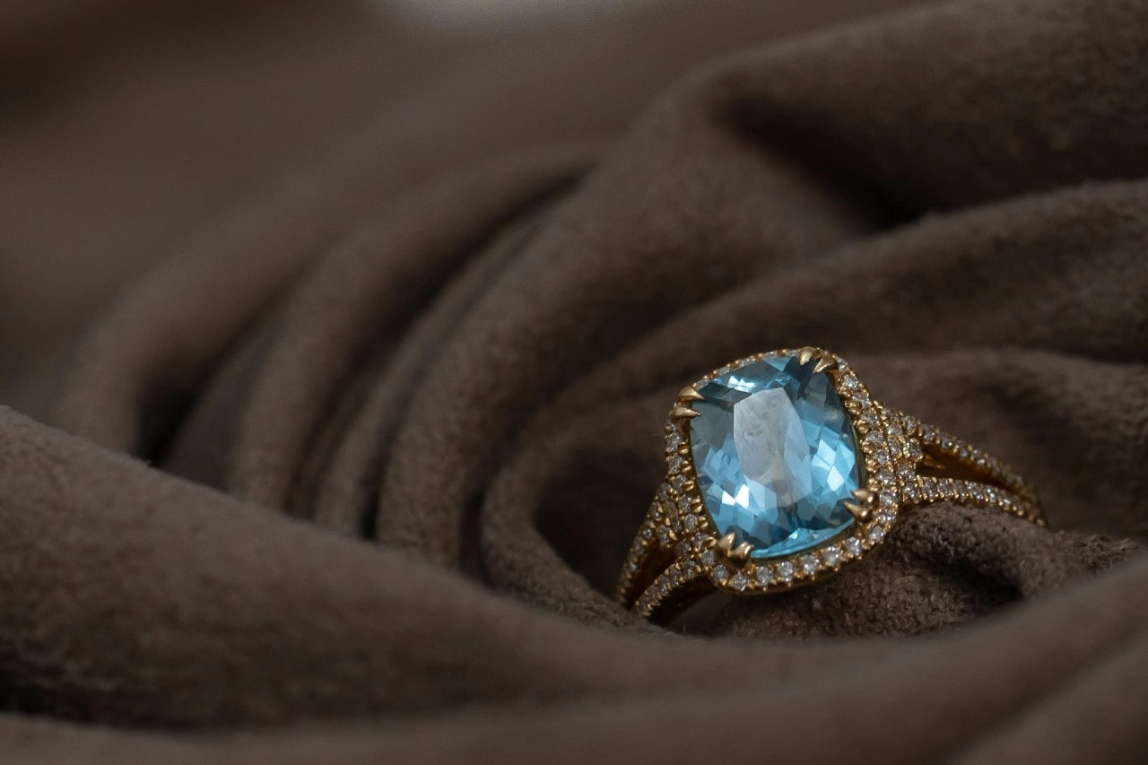 A gold ring with a large topaz center stone, surrounded by small diamonds placed on soft brown fabric.