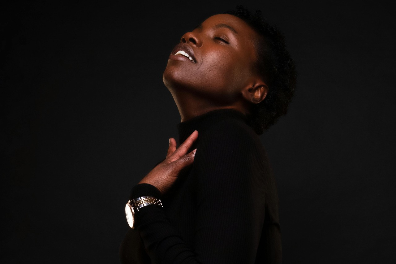 a woman wearing all black against a black background touching her neck and wearing a watch a woman wearing all black against a black background touching her neck and wearing a watch