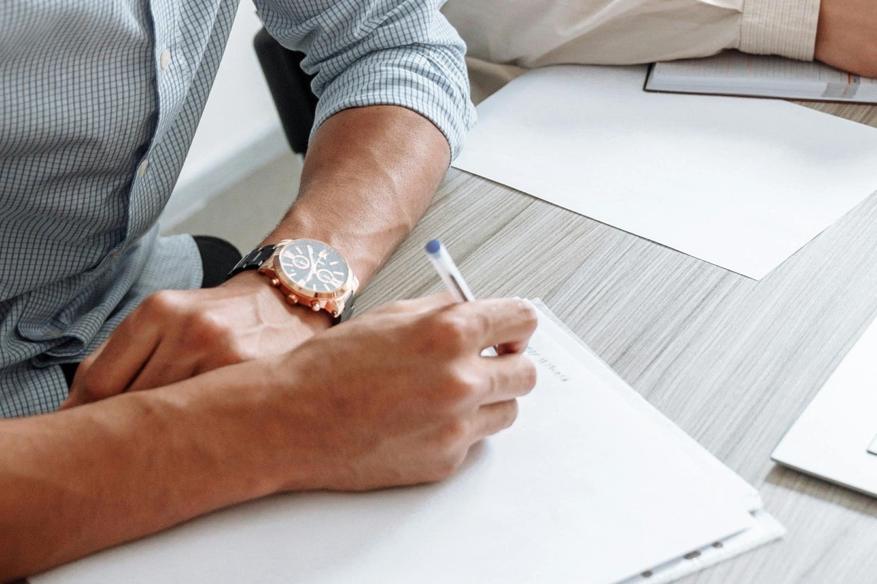 a business person writing on a pad and wearing a black and rose gold watch a business person writing on a pad and wearing a black and rose gold watch