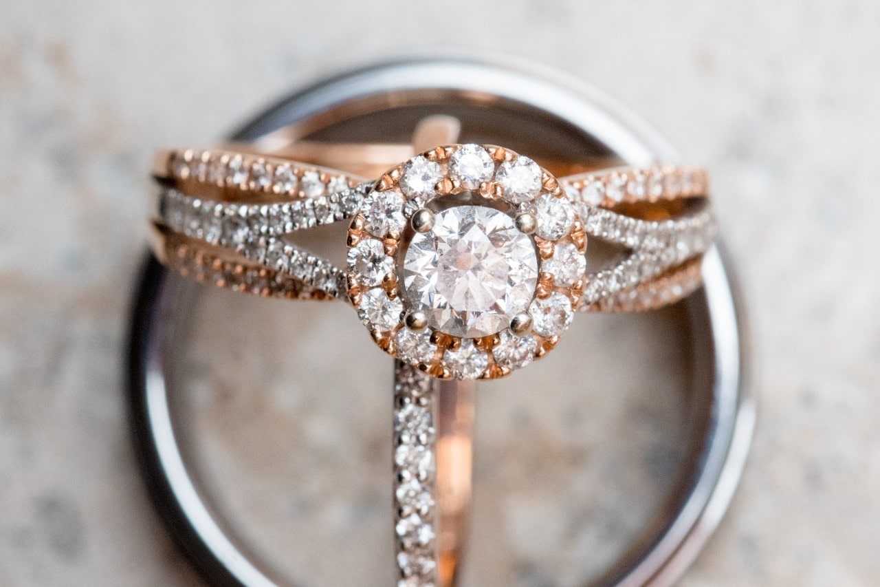 A rose gold diamond engagement ring with a round diamond center stone surrounded by a sparkling halo and encrusted with smaller diamonds A rose gold diamond engagement ring with a round diamond center stone surrounded by a sparkling halo and encrusted with smaller diamonds